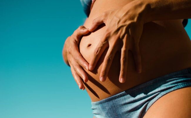 femme enceinte pose ses mains encoeur autour de son nombril